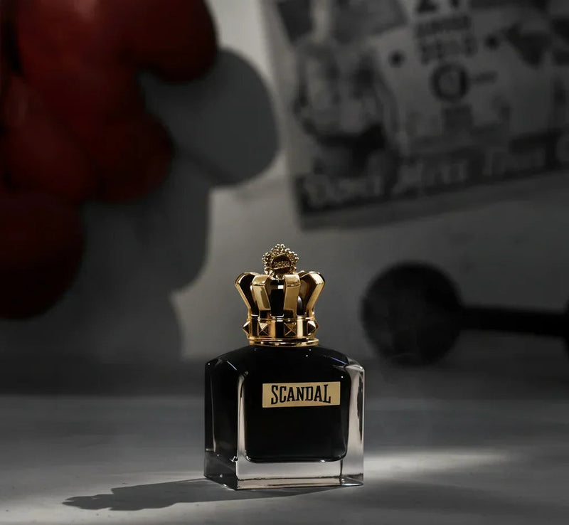 Frasco de perfume Scandal preto com tampa dourada em formato de coroa, cenário sombrio