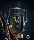 Frasco de perfume masculino preto com letra V dourada, bolhas e fava de baunilha ao fundo