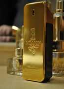 Frasco de perfume 1 Million dourado sobre mesa, com outros frascos ao fundo, destaque elegante.
